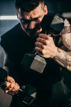 Focused athlete lifting dumbbells in gym, showcasing strength and tattoos.