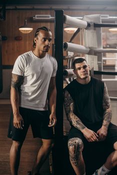 Serious multiracial men in casual wear with tattoos looking away in wooden house with glowing lights