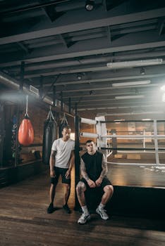 Two athletic men relaxing in a boxing gym with punching bags. Fit and focused.