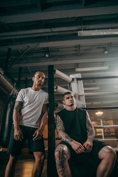 Two athletic men taking a break in a boxing gym, exuding strength and focus.