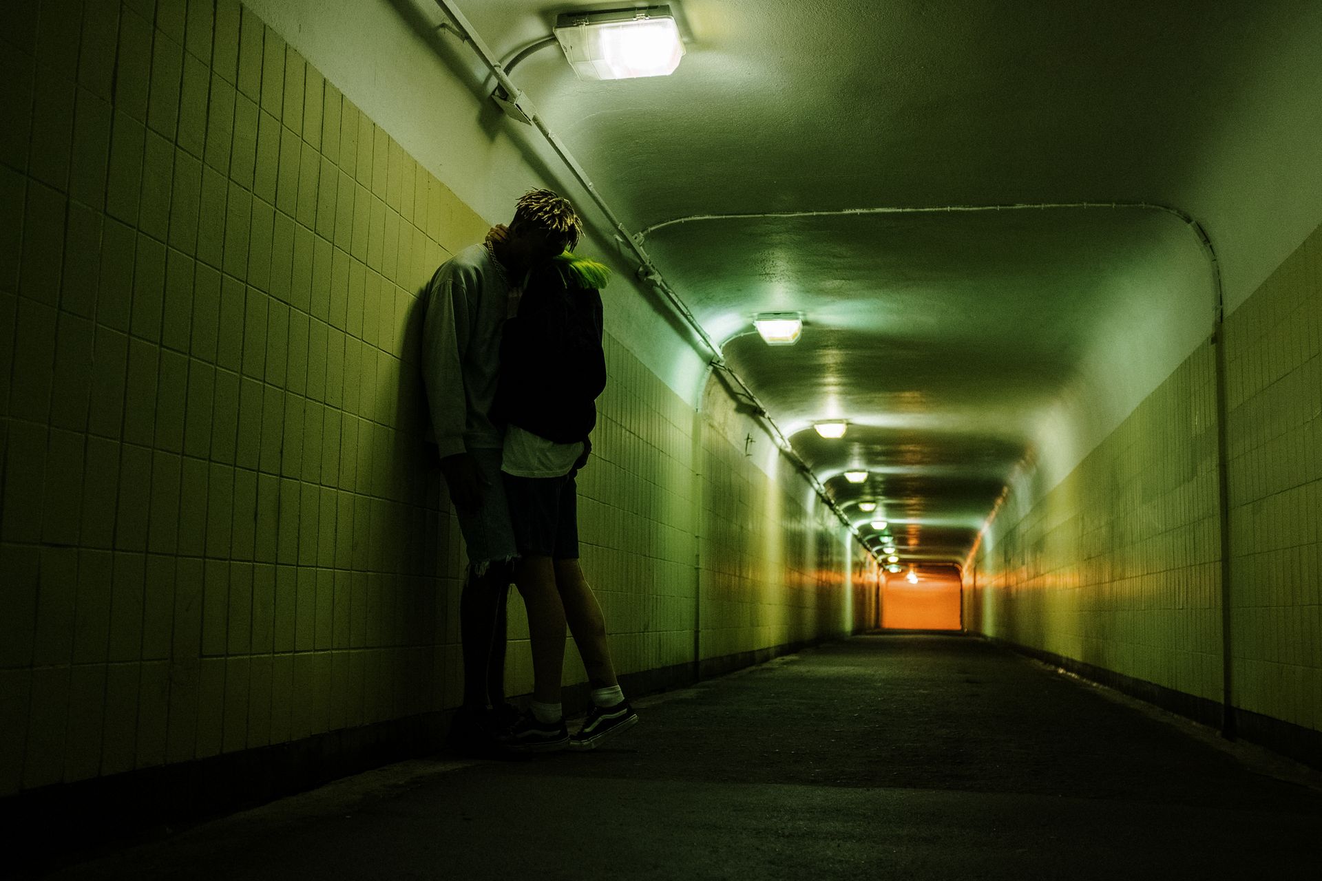 A young couple embraces under fluorescent lighting in an urban underground tunnel, creating a moody and intimate atmosphere.