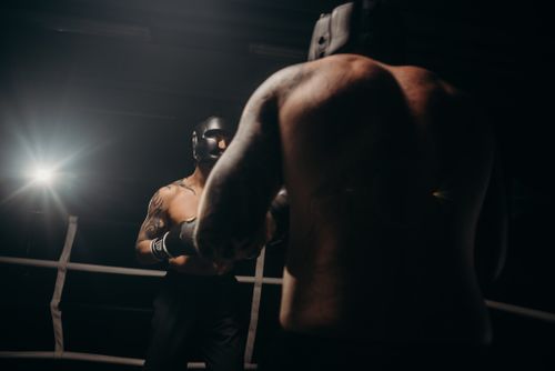 Free Two boxers sparring in a dimly lit gym, wearing head guards for protection. Stock Photo