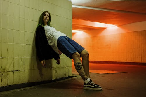 Kostenlos Frau In Der Schwarzen Jacke Und In Den Blauen Jeans, Die An Die Wand Lehnen Stock-Foto