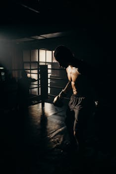 Silhouetted male boxer trains with dramatic lighting, emphasizing strength and focus.