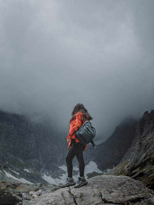 Woman in Orange Jacket Standing on a Rock