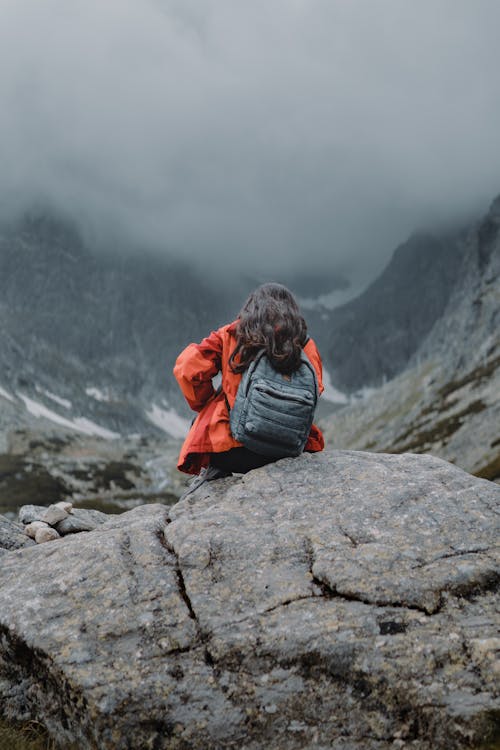 Person in Orange Jacket Sitting on a Rock