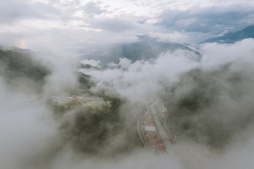 高空航拍下，云雾覆盖的山谷中道路蜿蜒，建筑物散落其间