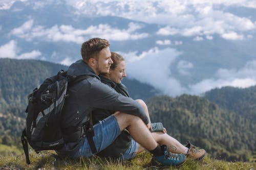 A Couple Embracing while Sitting on the Top of the Mountain