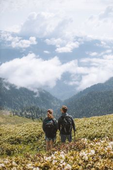 在多云天空下，两名背包客欣赏着风景优美的山景