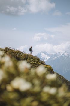 一名孤独的徒步旅行者站在郁郁葱葱的小山上，背后是白雪皑皑的山脉，天空明亮