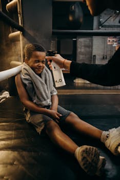 A child boxer gets sprayed with water during a training break inside a gym.