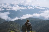 在多云的天空下，两名徒步旅行者欣赏着令人惊叹的山景，拥抱冒险