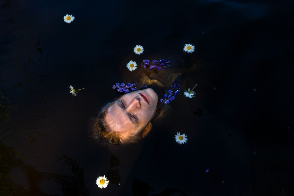 High angle of young male swimming in dark water and keeping head on surface with fresh flowers