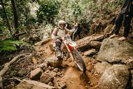 Energetic male biker in helmet riding mountain motorbike on rough stony terrain in tropical forest