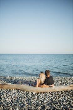 A couple enjoying a serene sunset on a rocky beach, embracing the romantic ambiance.
