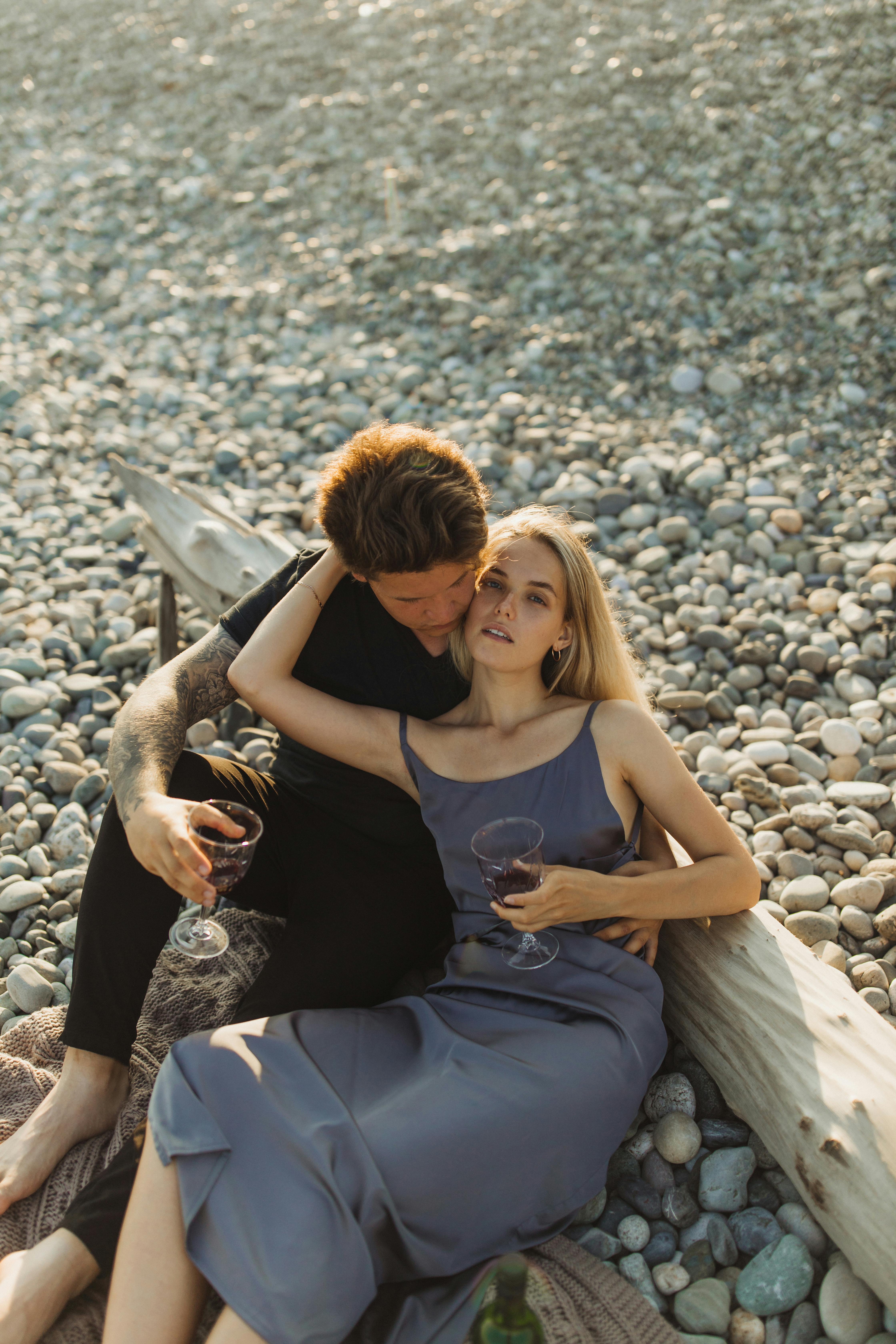 A loving couple enjoying each other's company with wine on a picturesque pebble beach.