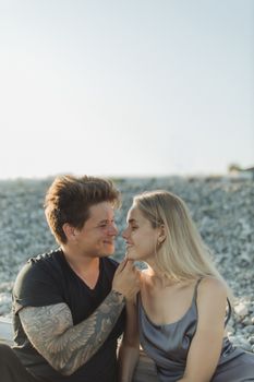 一对夫妇坐在鹅卵石海滩上，浪漫地凝视着彼此的双眼