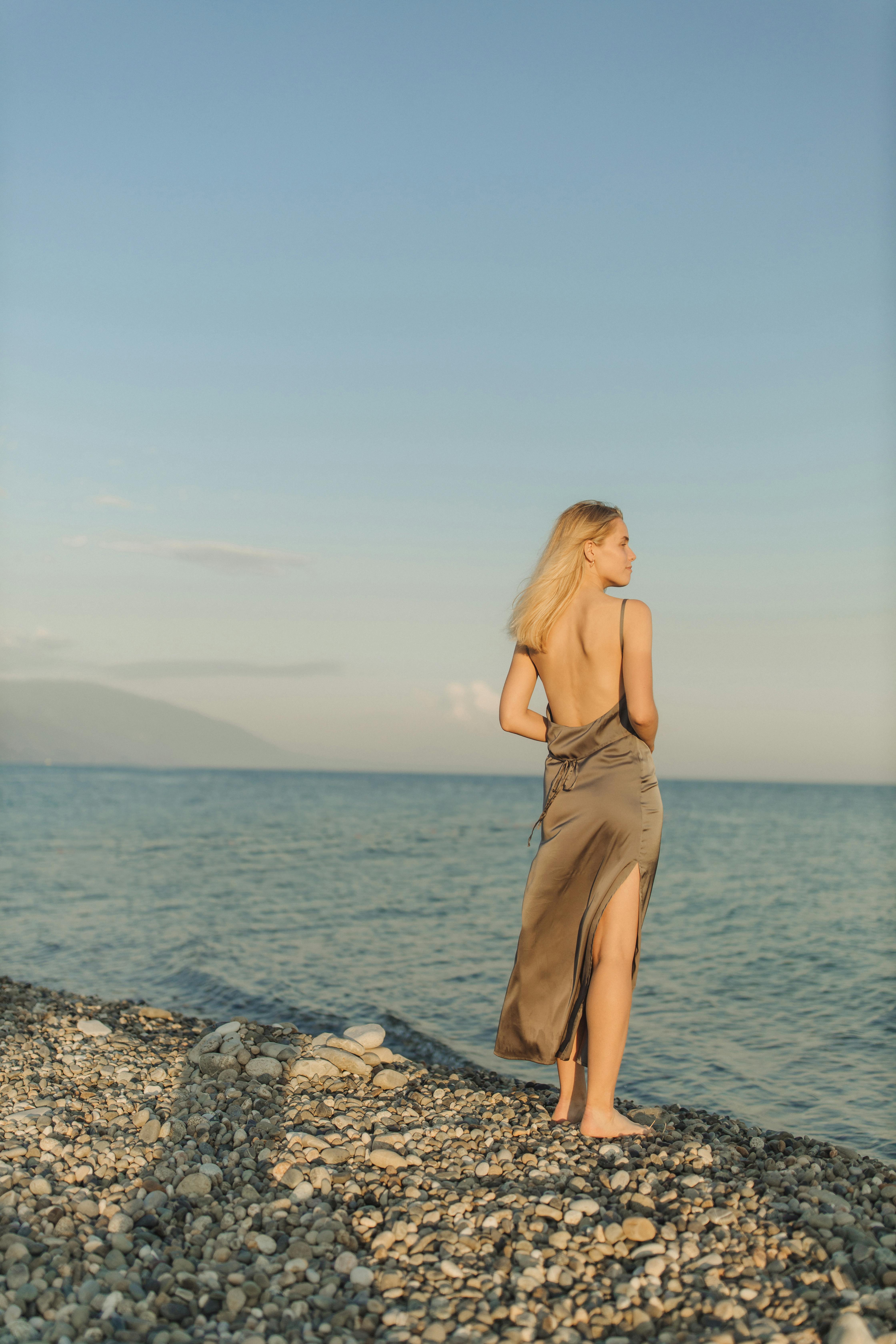woman in brown spaghetti strap dress standing on rocky shore