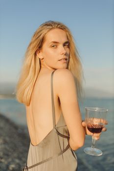 一名女子端着酒杯，在海滩上享受宁静的日落