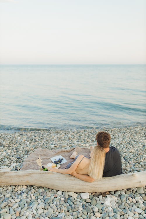 Free Woman in White Tank Top Sitting on Gray Rock Near Body of Water Stock Photo