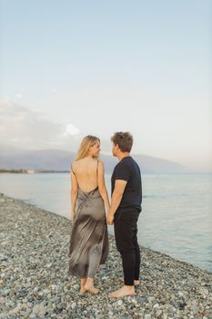 日落时分，一对情侣手牵着手，漫步在海边的鹅卵石海滩上