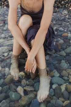 A woman sits with her feet in rocky beach waters, enjoying a serene moment.