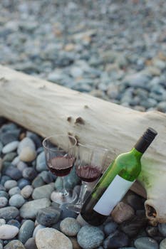 Elegant wine setting on a pebble beach with driftwood, perfect for romantic occasions.