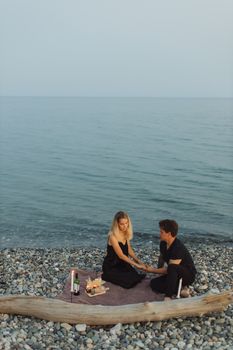 一对夫妇在鹅卵石海滩上，伴着葡萄酒和蜡烛，享受日落野餐，营造出浪漫的氛围