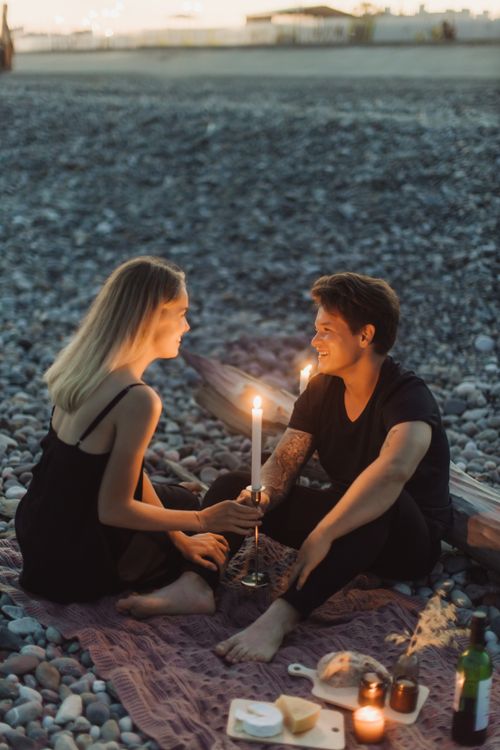 Free A couple enjoying a romantic beach picnic by candlelight at sunset. Stock Photo