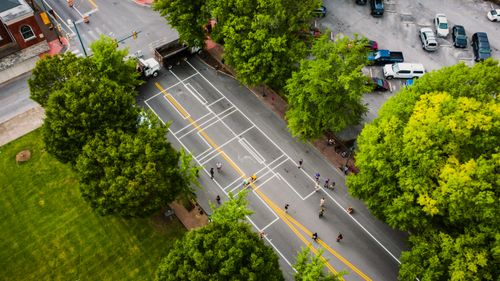 Free Aerial view of roadway with marking lines and unrecognizable people between meadow with bright trees and parking in city Stock Photo