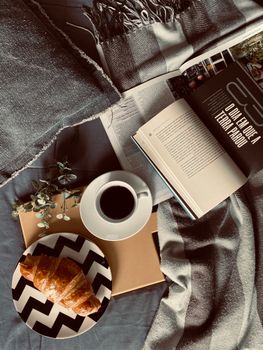 Top view of a cozy breakfast setup with coffee, croissant, and an open book.