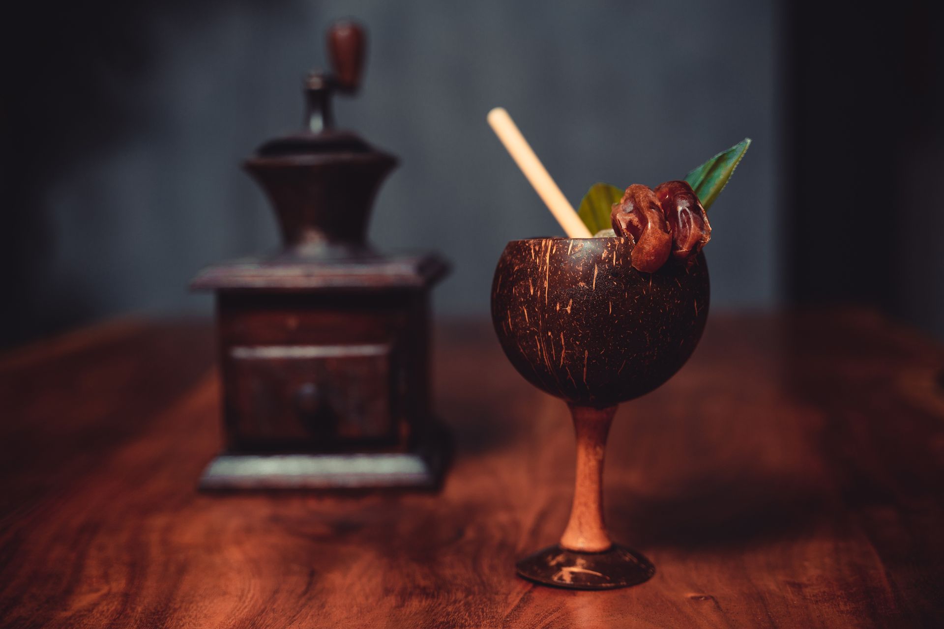 Exotic cocktail served in a coconut shell goblet with a date and leaf garnish, set on a rustic wooden table.