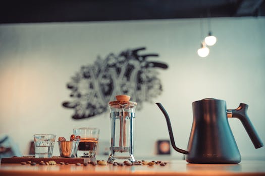 Elegant coffee arrangement with a French press, kettle, glasses, and coffee beans on a table.