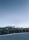 Picturesque view of snowy mountain range behind green forest and clope with ski lift under clear sky