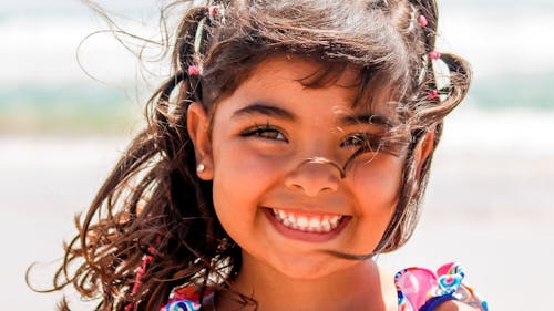 Free Crop adorable cheerful ethnic little girl with dark hair smiling and looking at camera on sunny day Stock Photo