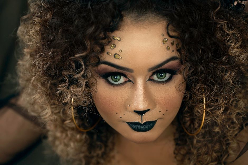 Close-up portrait of a woman with fierce cat-inspired makeup and curly hair, emphasizing her bold style.