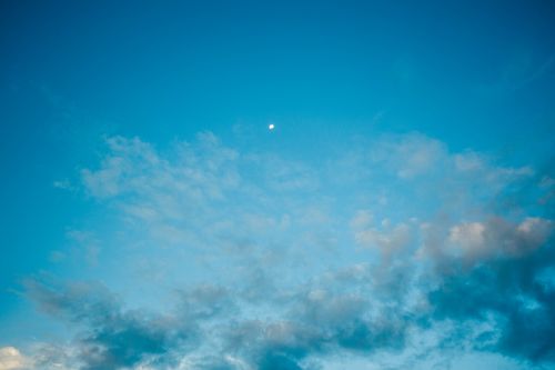 Free Tiny Moon in amazing vibrant blue sky covered with highlighted clouds in evening Stock Photo