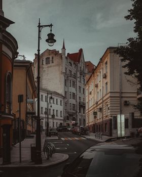 Old buildings located near road with cars on street of historic city on cloudy day