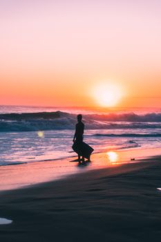 A silhouette of a person with a bodyboard on Carcavelos Beach during a vibrant sunset.