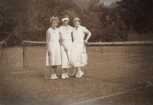 A classic vintage photo of three women on a tennis court holding rackets.
