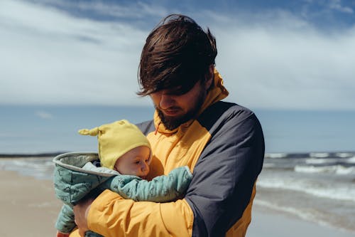 Free Man in Yellow W indbreaker Carrying Baby in Yellow Hat Stock Photo