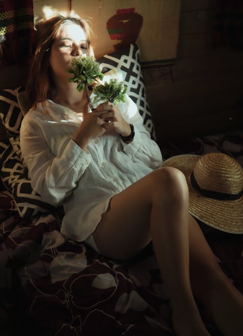 Woman in White Shirt and Black Skirt Sitting on Floral Sofa and Sniffing Flower
