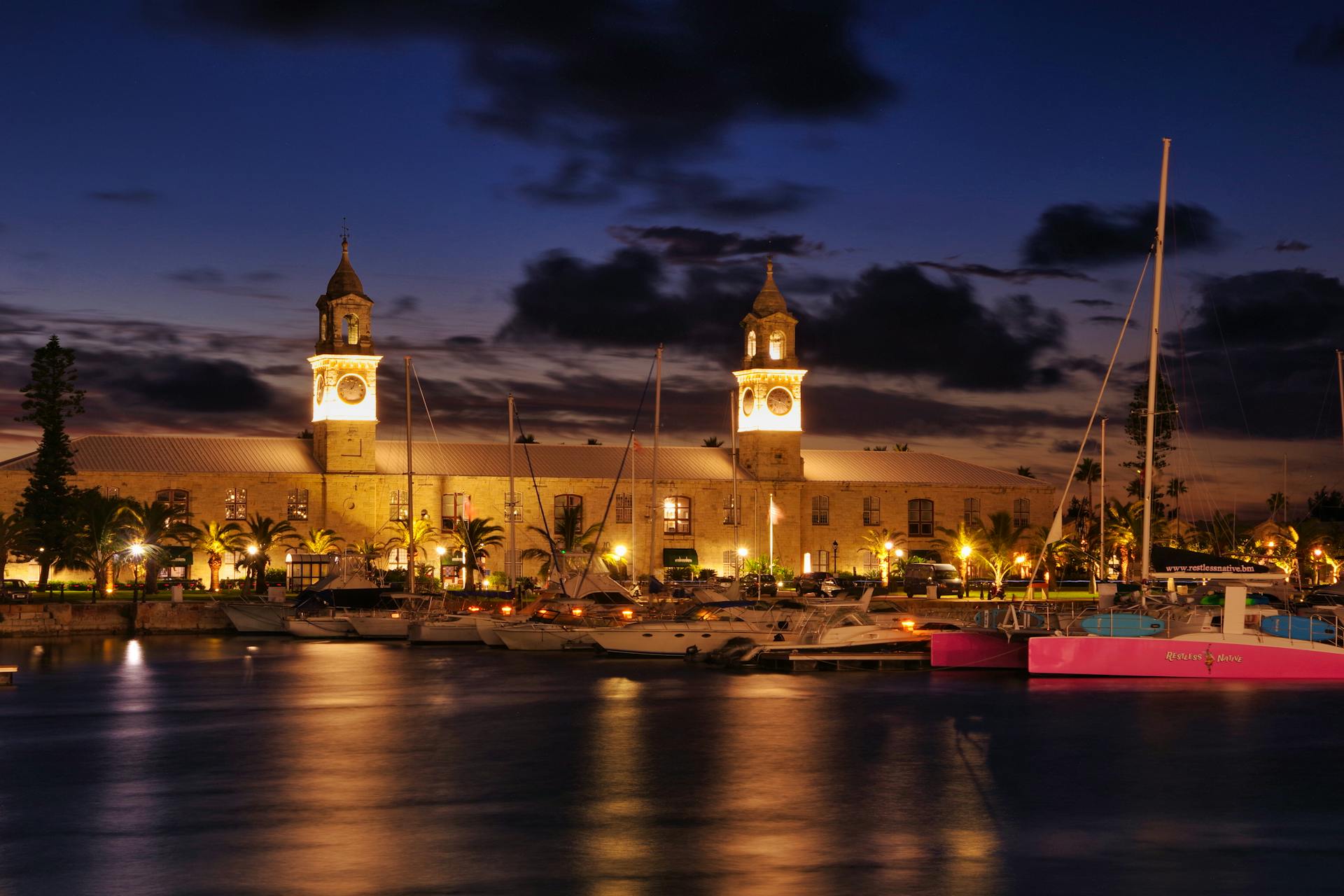 A stunning nighttime view of the Royal Navy Shipyard in Bermuda with illuminated clock towers and yachts.