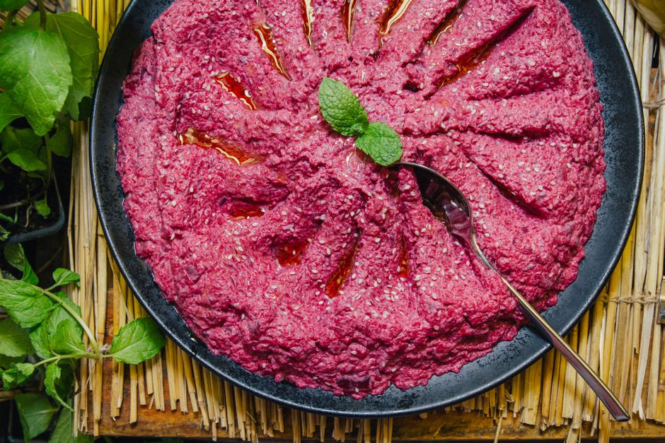 A swirl of vivid pink beet hummus in a shallow bowl, topped with a drizzle of olive oil, sesame seeds, and fresh dill.