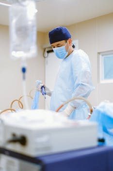 A surgeon in full scrubs and face mask operating in a sterile hospital environment.