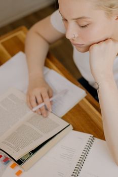 一位穿着休闲装、神情专注的年轻女子正坐在办公桌前，翻开书籍和笔记学习