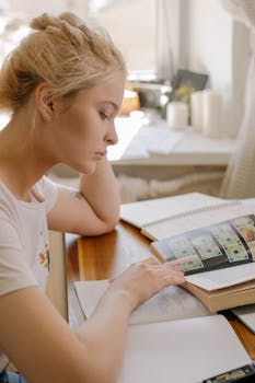 Focused young woman studying at home by the window with books open, illustrating a learning environment.