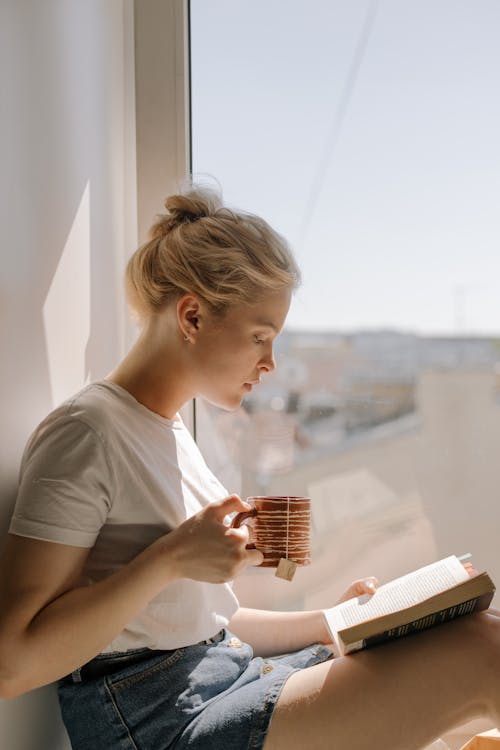 Woman in White Crew Neck T-shirt Holding Book