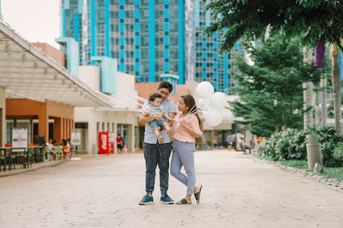 Man Carrying Their Son while the Woman Holding White Balloons