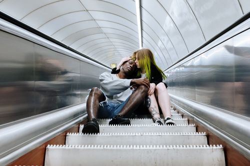 Free A modern couple shares a tender moment on a subway escalator, symbolizing urban romance. Stock Photo